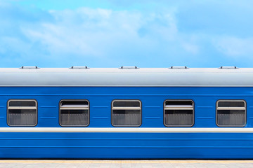 Blue passenger railway wagon on the platform, blue sky in the background