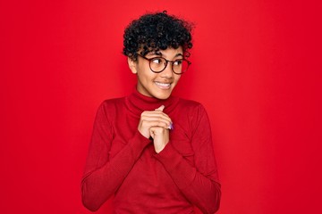 Fototapeta na wymiar Young beautiful african american afro woman wearing turtleneck sweater and glasses laughing nervous and excited with hands on chin looking to the side