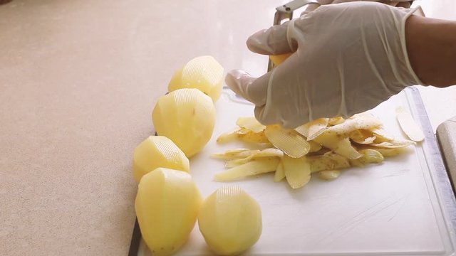 Close-up of a man in white gloves peeling potatoes to make fries, timelapse, hygiene in home kitchen during corona virus