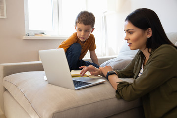 Cute little boy and his mother using laptop at home