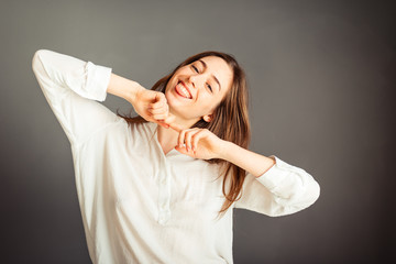 Fototapeta premium Young girl in a white shirt, hands up, on a gray background. Honest and emotional on the banner, billboard, billboard. No retouch. Without make-up.