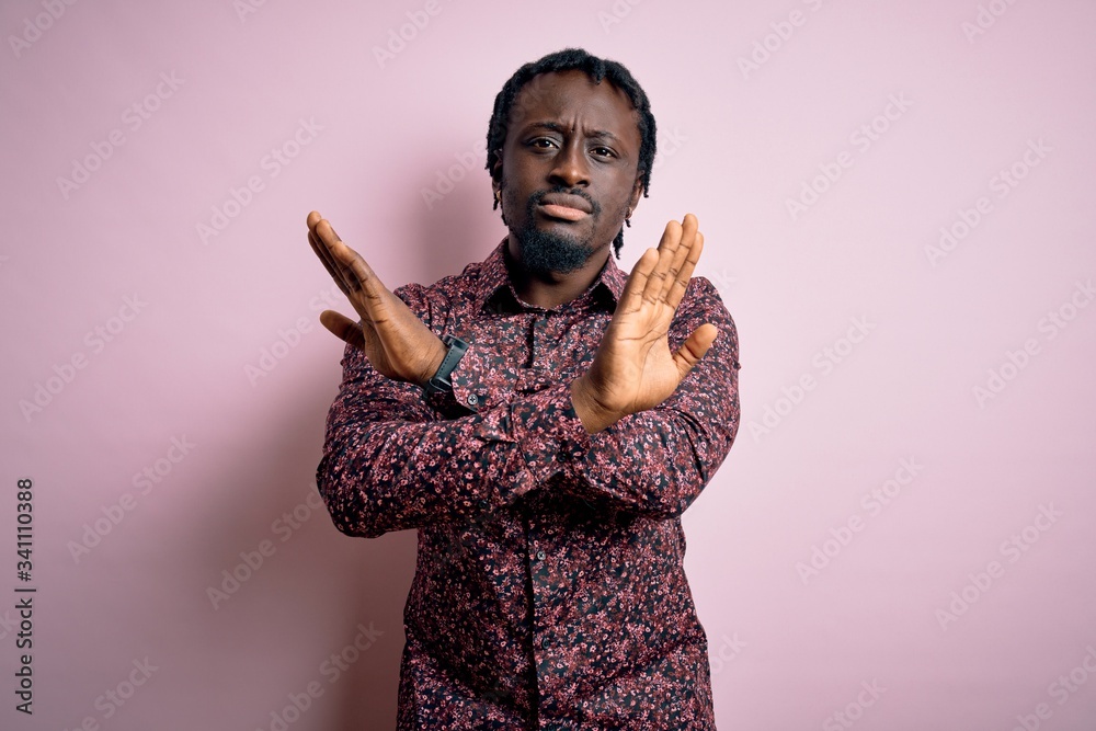 Poster Young handsome african american man wearing casual shirt standing over pink background Rejection expression crossing arms doing negative sign, angry face