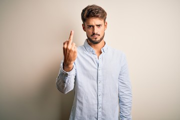 Young handsome man with beard wearing striped shirt standing over white background Showing middle finger, impolite and rude fuck off expression