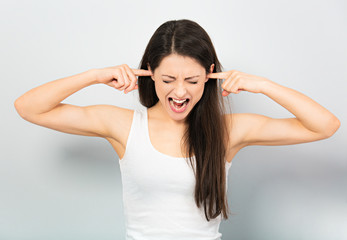 Anger young casual woman strong screaming with wild open mouth and covering the ears the fingers on blue background. Closeup