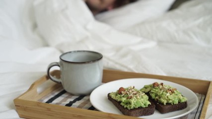 Male having breakfast avocado toast specialty coffee in bed on tray. Handsome hipster man wakes up and drink coffee, enjoys home mode