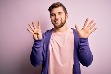 Naklejka premium Young blond man with beard and blue eyes wearing purple sweatshirt over pink background showing and pointing up with fingers number nine while smiling confident and happy.