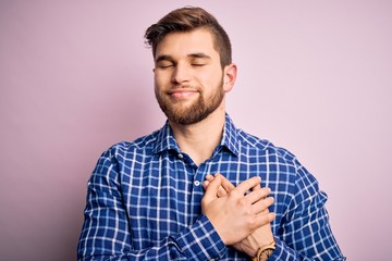 Young handsome blond man with beard and blue eyes wearing casual shirt standing smiling with hands on chest with closed eyes and grateful gesture on face. Health concept.
