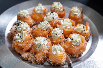 Rolls of salmon with cream cheese, laid out on a silver plate.