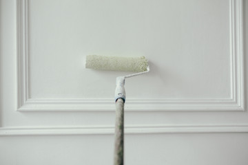 Close-up. Painting and repair of a decorative wall in white color with a construction roller. Construction tools.