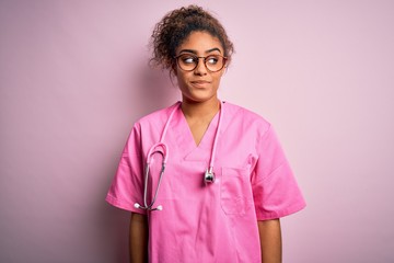 African american nurse girl wearing medical uniform and stethoscope over pink background smiling...