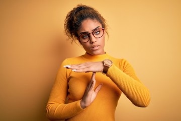 Young beautiful african american girl wearing sweater and glasses over yellow background Doing time...
