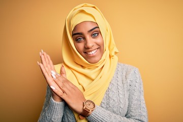 Young beautiful african american girl wearing muslim hijab over isolated yellow background clapping and applauding happy and joyful, smiling proud hands together