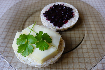 Homemade goat cheddar slices and blackcurrant jam on puffed rice rounds on plate