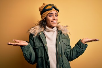 Young african american afro skier girl wearing snow sportswear and ski goggles smiling showing both hands open palms, presenting and advertising comparison and balance