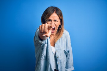 Middle age beautiful woman wearing casual shirt standing over isolated blue background pointing displeased and frustrated to the camera, angry and furious with you