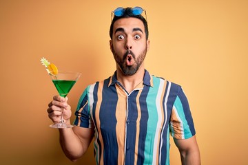 Young handsome tourist man with beard on vacation wearing summer shirt drinking cocktail scared in shock with a surprise face, afraid and excited with fear expression