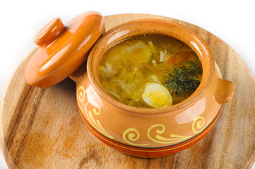 Noodle soup with chicken and quail egg in a pot on round wooden Board view closeup