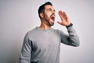 Young handsome man with beard wearing casual sweater standing over white background shouting and screaming loud to side with hand on mouth. Communication concept.