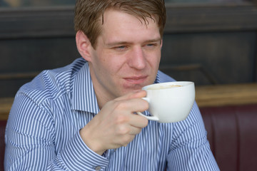 Face of young blond businessman thinking and drinking coffee