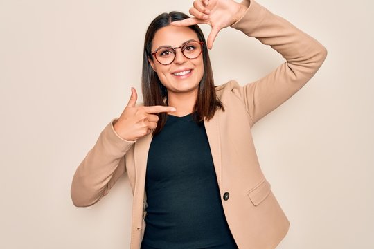 Young beautiful brunette businesswoman wearing jacket and glasses over white background smiling making frame with hands and fingers with happy face. Creativity and photography concept.