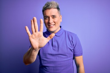 Naklejka premium Young handsome modern man wearing casual purple t-shirt over isolated background showing and pointing up with fingers number five while smiling confident and happy.