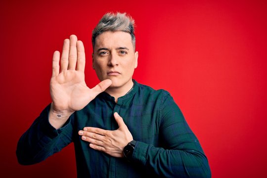 Young handsome modern man wearing elegant green shirt over red isolated background Swearing with hand on chest and open palm, making a loyalty promise oath