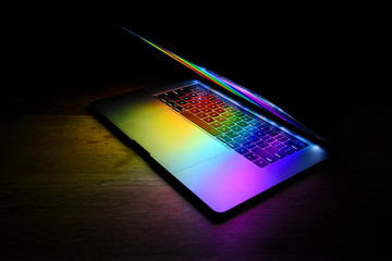 Open laptop isolated on dark wooden table with rainbow colors reflecting on keyboard - Powered by Adobe
