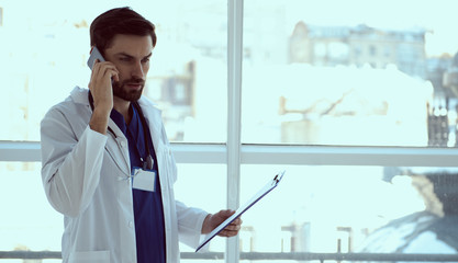 Serious doctor taking on cellphone and holding clipboard