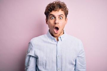 Obraz premium Young blond handsome man with curly hair wearing striped shirt over white background afraid and shocked with surprise and amazed expression, fear and excited face.