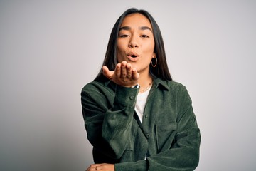 Young beautiful asian woman wearing casual shirt standing over isolated white background looking at the camera blowing a kiss with hand on air being lovely and sexy. Love expression.