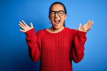 Young beautiful asian woman wearing casual sweater and glasses over blue background celebrating mad...
