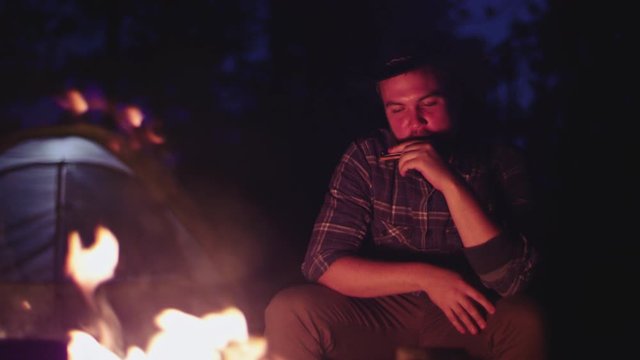 Cowboy plays the harmonica by a campfire at night in slow motion