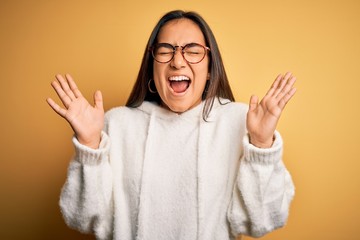 Young beautiful asian woman wearing casual sweater and glasses over yellow background celebrating...