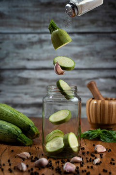 zucchinis o zapallitos volando cayendo en un frasco de conserva con los ingredientes     ajo pimienta y mortero de madera