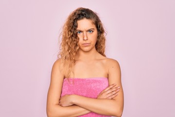 Obraz na płótnie Canvas Beautiful blonde woman with blue eyes wearing towel shower after bath over pink background skeptic and nervous, disapproving expression on face with crossed arms. Negative person.