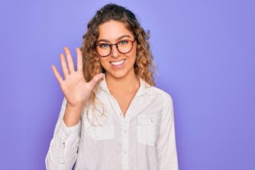 Young beautiful woman with blue eyes wearing casual shirt and glasses over purple background showing and pointing up with fingers number five while smiling confident and happy.