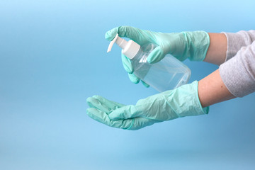 Female hands in rubber gloves squeeze hand sanitizer gel from bottle on blue background. Hand...