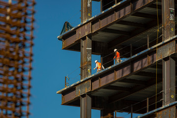 Close up of commercial office building under construction with construction workers ,steel beams,land rebar.  The scene is against a blue sky