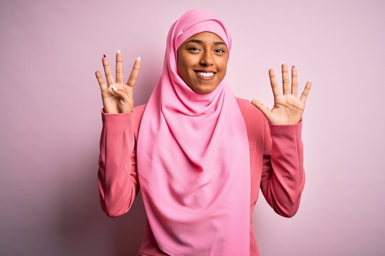 Young African American afro woman wearing muslim hijab over isolated pink background showing and pointing up with fingers number nine while smiling confident and happy.