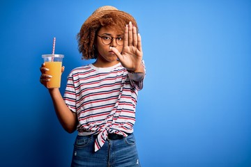 Young African American woman with curly hair on vacation wearing hat drinking orange juice with...