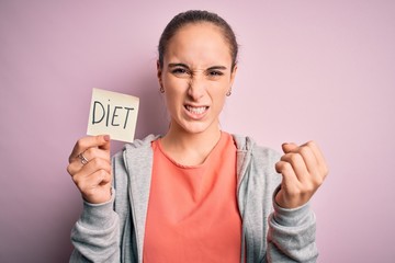 Young beautiful sporty woman doing sport holding reminder paper with diet message annoyed and frustrated shouting with anger, crazy and yelling with raised hand, anger concept