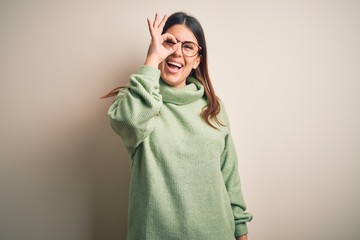 Young beautiful woman wearing casual sweater standing over isolated white background doing ok gesture with hand smiling, eye looking through fingers with happy face.