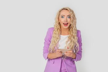 Surprised, excited, beautiful blonde curly woman playing a game for a smartphone, holding a mobile phone in a horizontal position