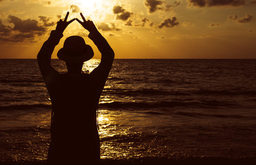 Silhouette of Happy man standing with showing 2 fingers while sunset at sea,Light flare,Enjoys of resting time,Freedom concept