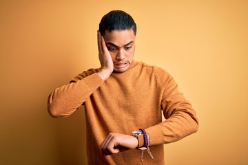 Young brazilian man wearing casual sweater standing over isolated yellow background Looking at the watch time worried, afraid of getting late