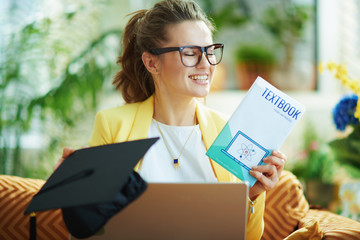 Fototapeta premium happy modern woman with graduation cap, laptop and textbook