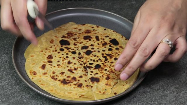 Woman hands cutting Indian grated Cauliflower stuffed flatbread Paratha on a skillet.
