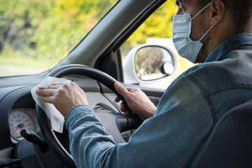 Caucasian man wearing face mask cleaning the steering wheel with a wipe. Covid-19 concept