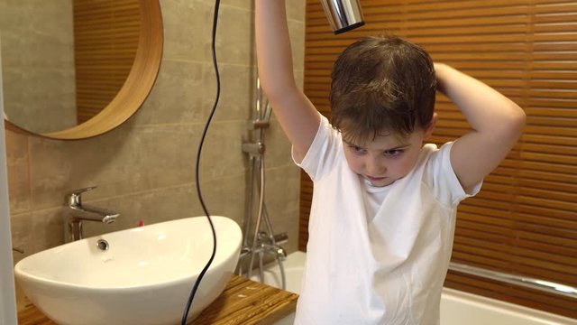 Child with a hairdryer. The little boy funny dries wet hair with a hairdryer