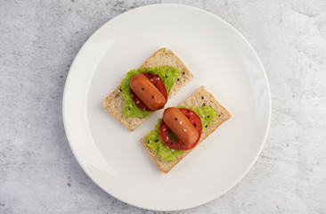 Sausage with tomatoes, salad and two sets of bread on a white plate.